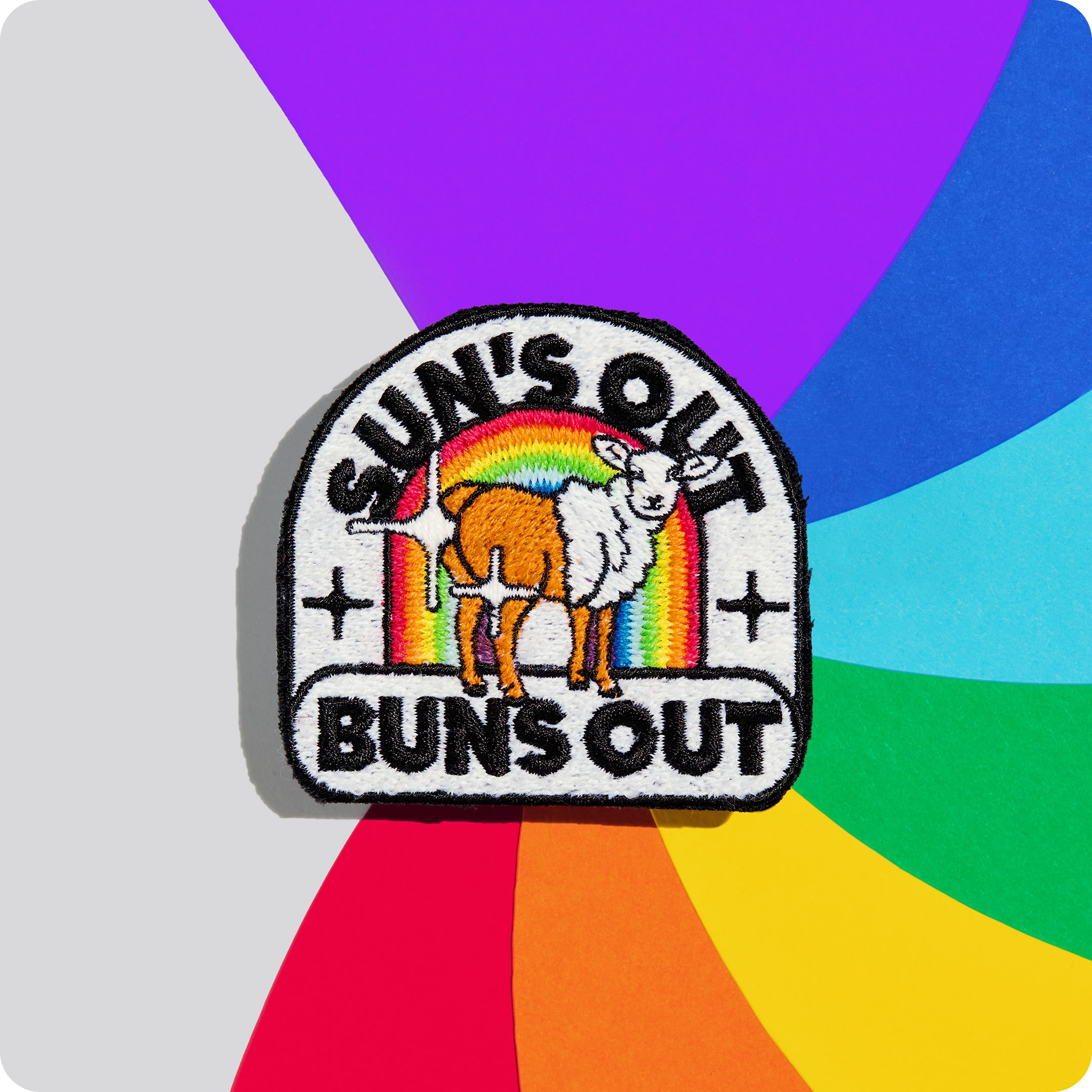 Patch "sun's out buns out" aus schwuler Schafwolle auf einem bunten Hintergrund.