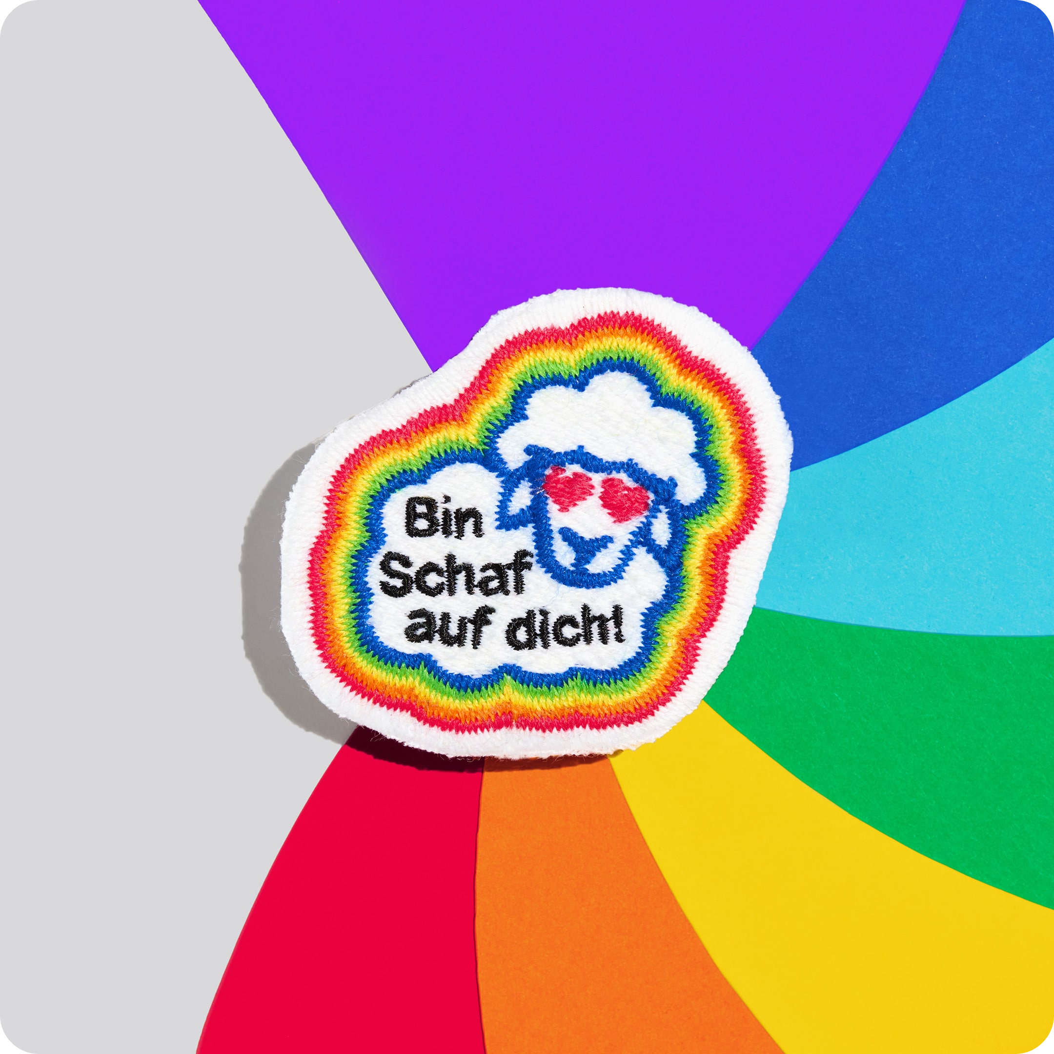 Patch "Bin Schaf auf dich!" aus schwuler Schafwolle auf einem bunten Hintergrund.