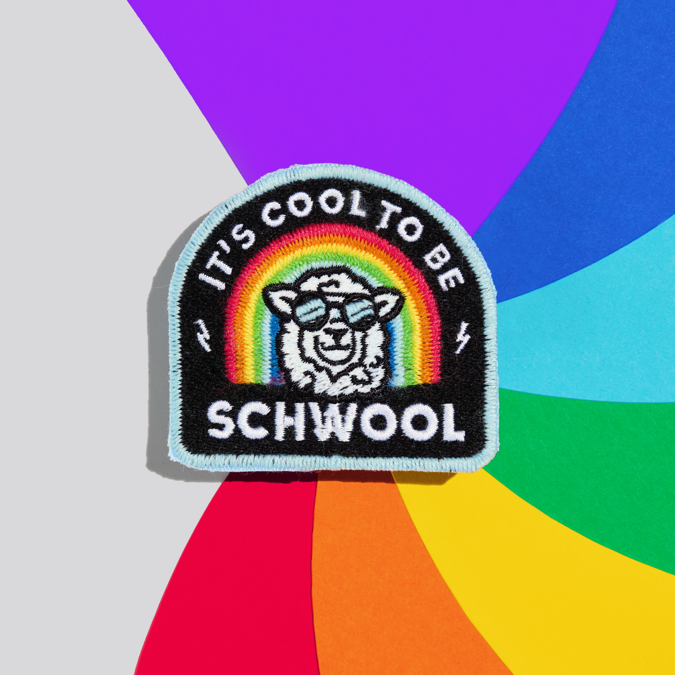 Patch "It's cool to be schwool" aus schwuler Schafwolle auf einem bunten Hintergrund.