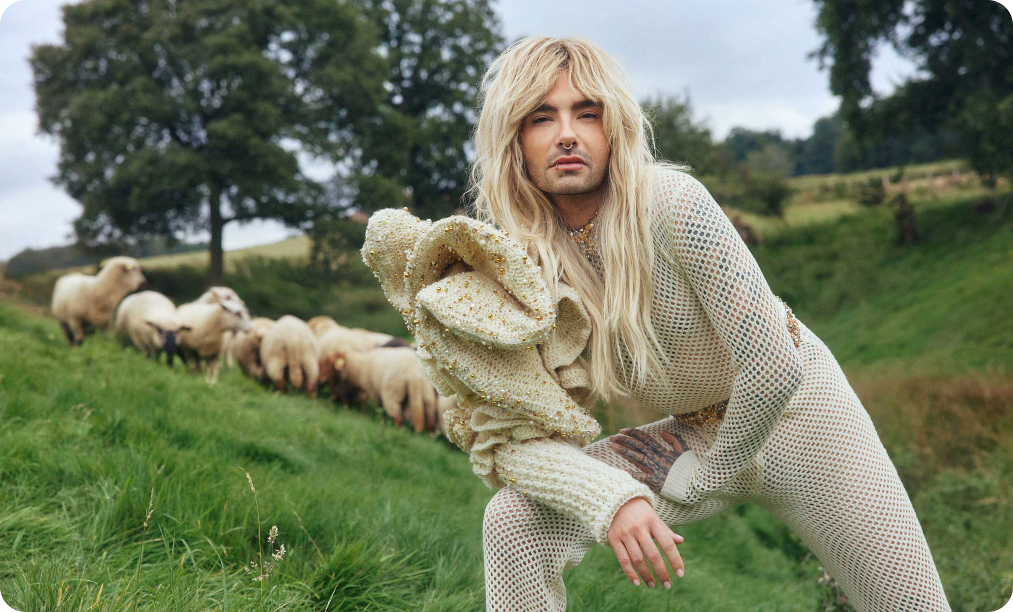 Bill Kaulitz posing on a meadow in front of a flock of gay sheep.