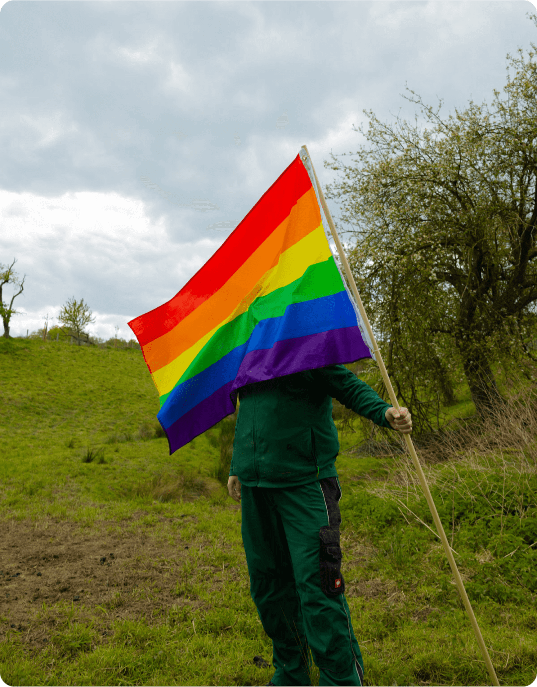 Mann hält auf einer Wiese eine Regenbogenflagge.