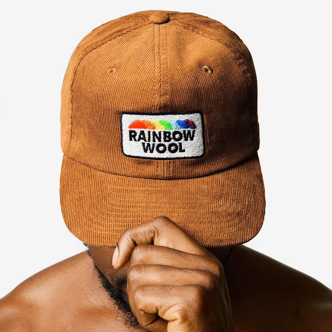 "Rainbow Wool" Corduroy Cap with a logo motif made of gay sheep wool on a male model’s head.