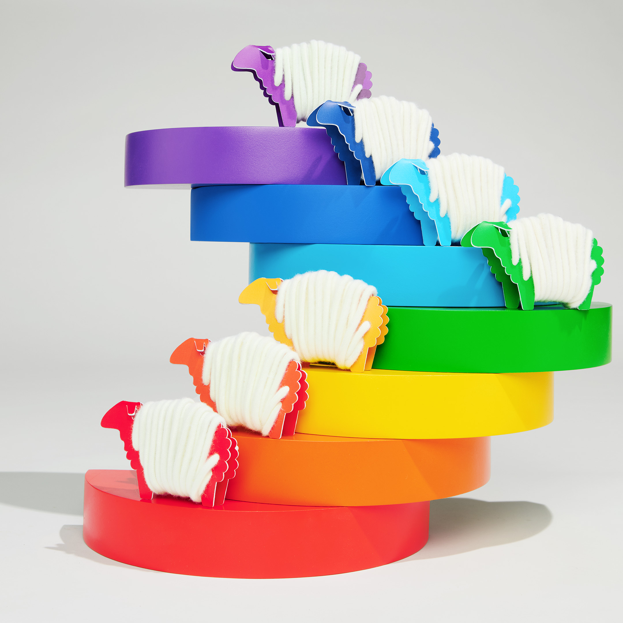 Rainbow Wool Laces made of gay sheep wool wrapped around multiple colorful paper sheep  in front of a white  background.