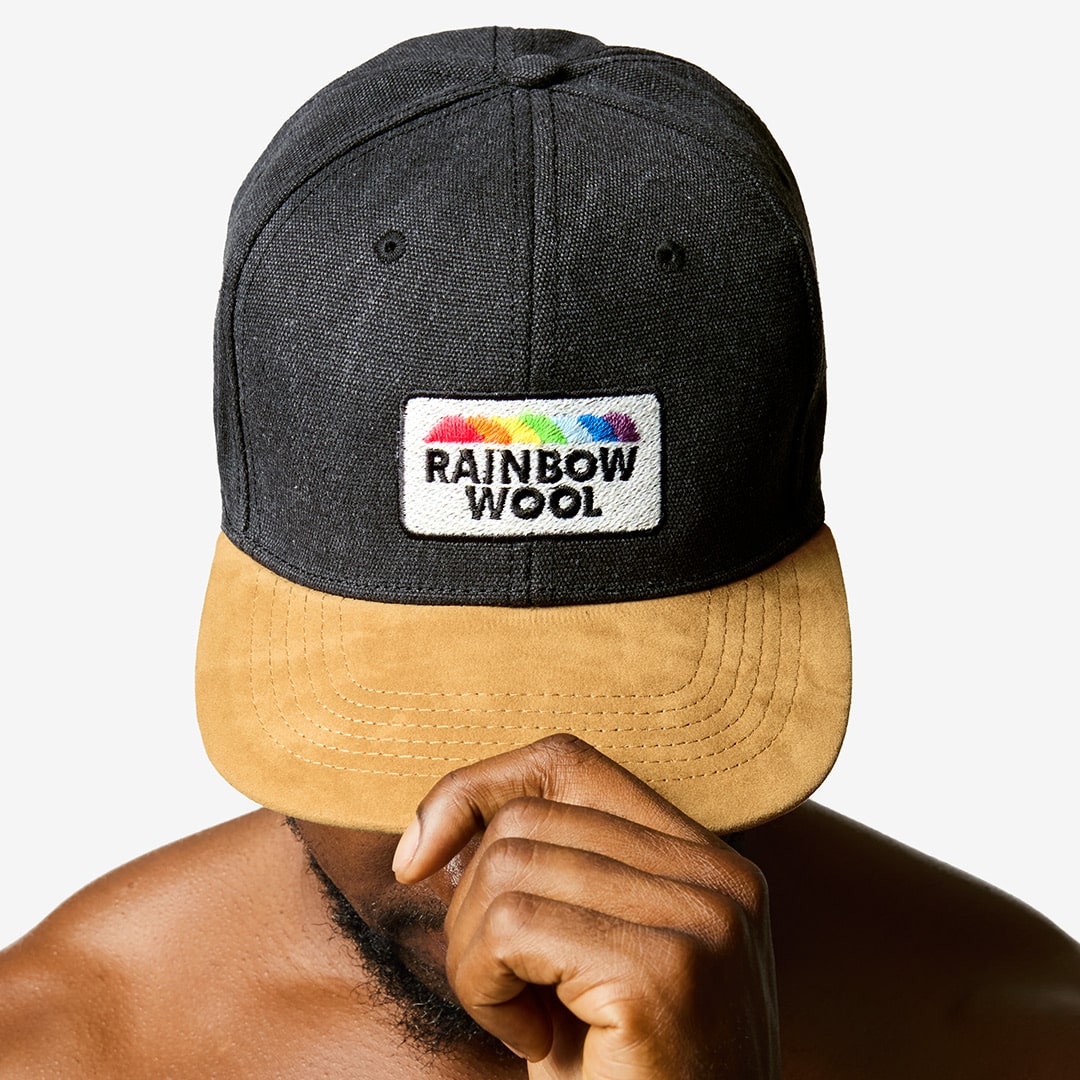 "Rainbow Wool" Skater Cap with a logo motif made of gay sheep wool on a male model’s head.