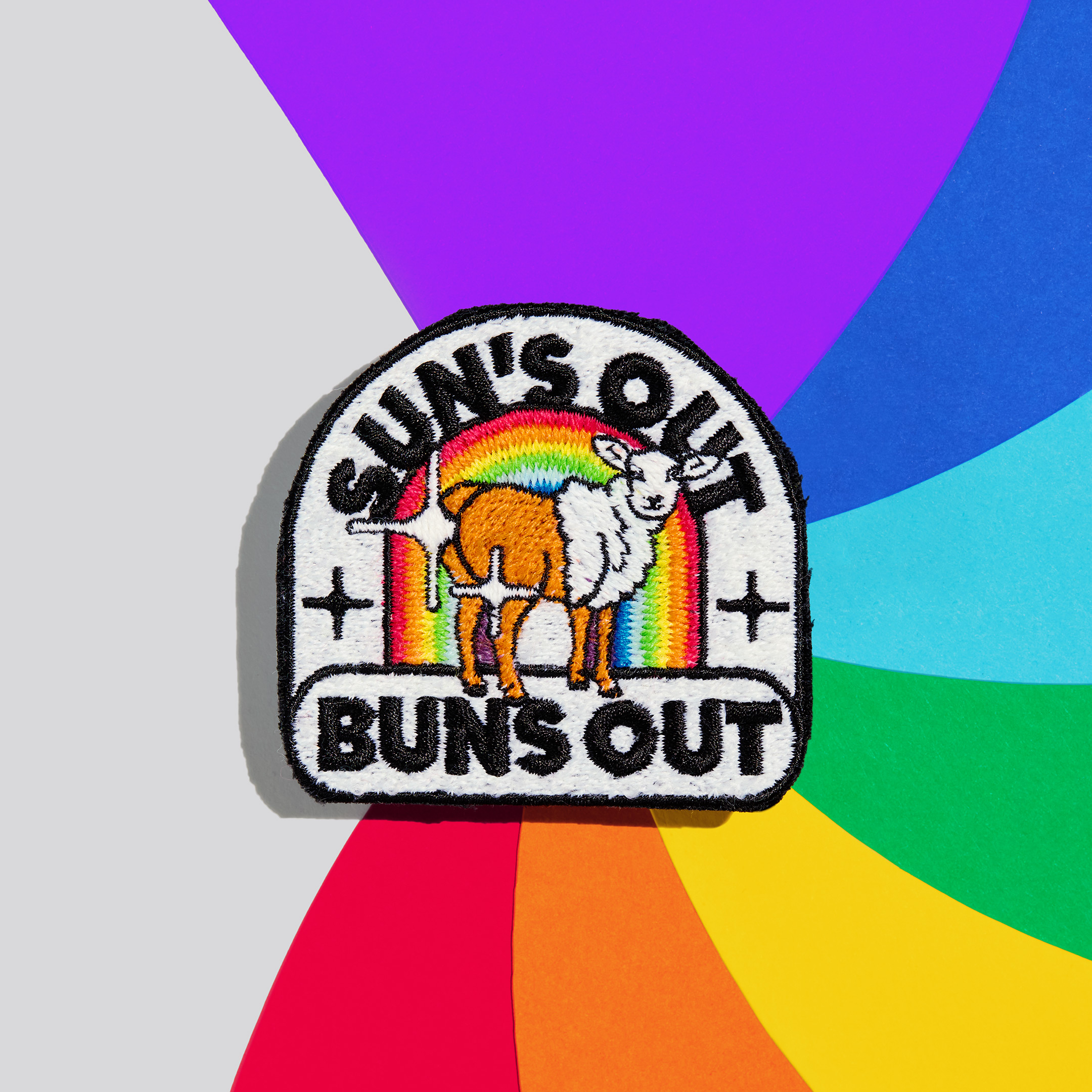 Patch "sun's out buns out" aus schwuler Schafwolle auf einem bunten Hintergrund.